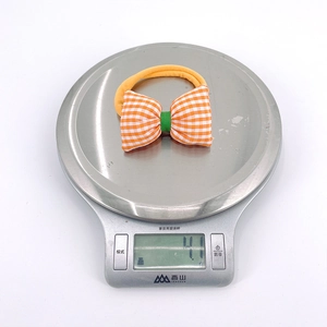 Close-up of lightweight orange plaid bow baby hairband weighing 4.1g on a scale