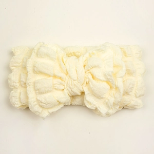 Close-up of cream baby headband featuring textured bubble fabric and a large bow design