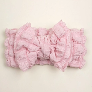 Close-up of pink oversized bow headband featuring soft seersucker pleated texture for babies