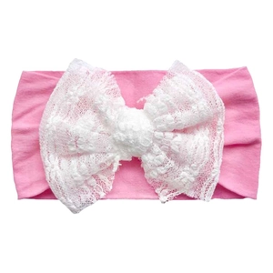 Detail of pink elastic headband featuring a large white lace bow for baby girls