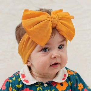 Detail of baby mustard yellow headband with large mesh bow on a model with floral shirt