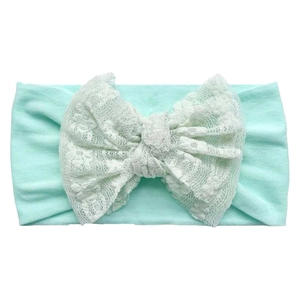 Detail of mint green baby headband with large creamy white floral lace bow on white background