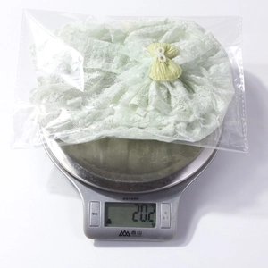 Detailed view showing lightweight 20.2g green lace baby headband on a weight scale