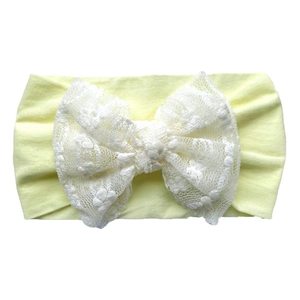 Detail of baby headband with oversized white lace bow on soft yellow elastic band