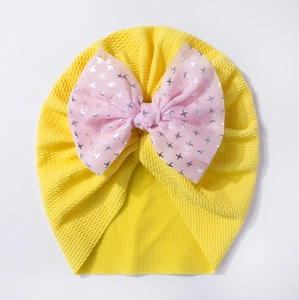 Detail of baby beanie with a large pink mesh bow and silver star prints on yellow fabric