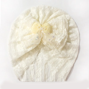 Close-up of white lace baby turban hat with yellow bow and sparkling star mesh detail