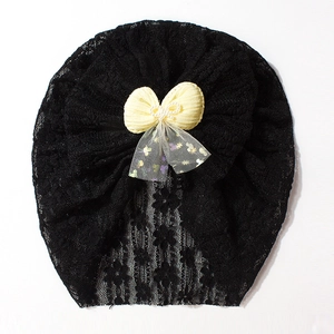Detail of hollow floral lace baby beanie with yellow bow and central pearl accent
