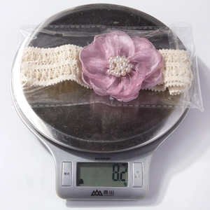 Détail d'un bandeau bébé en dentelle avec fleur sur une balance pesant 8,2g