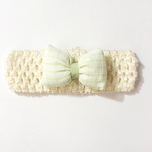 Détail d'un bandeau bébé au crochet avec un nœud à carreaux vert clair sur bande