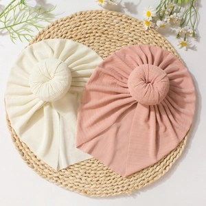 Detail of soft ribbed donut baby hats in cream and pink on a woven mat with daisies