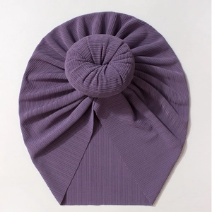 Macro detail of dark purple turban baby hat featuring a soft ribbed donut knot design