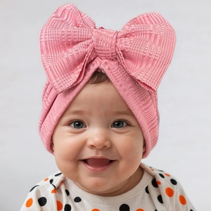 Vue détaillée d'un bonnet tricoté rose pour bébé avec un grand nœud 3D sur un nourrisson