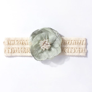 Détail d'un bandeau en dentelle pour bébé avec fleur en tissu vert et perles blanches