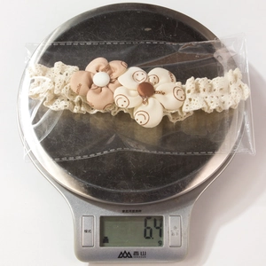 Detail showing 6.4g lightweight baby lace floral headband on a digital scale