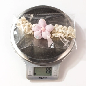 Vue détaillée d'un bandeau en dentelle pour bébé avec fleur en tissu rose et pompon