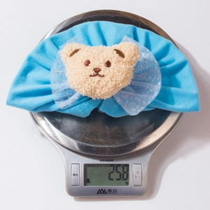 Détail d'un bonnet bleu pour bébé avec ours et nœud en tulle pesé sur une balance