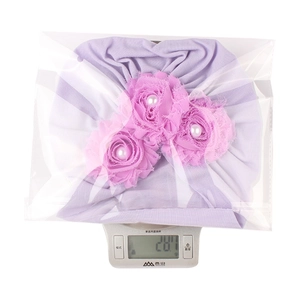 Mesure du poids d'un bonnet de bébé violet clair avec fleurs en mousseline et perles