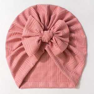 Vue détaillée du bonnet turban rose pour bébé avec texture côtelée et grand nœud décoratif