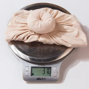 Detail shot of a soft knit newborn donut hat in skin pink weighing 31.0 grams on a scale