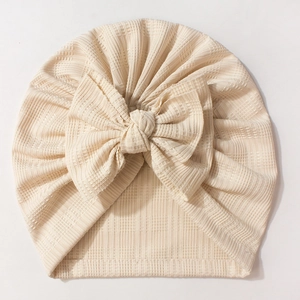 Détail du turban pour bébé montrant la texture en maille crème et le grand nœud