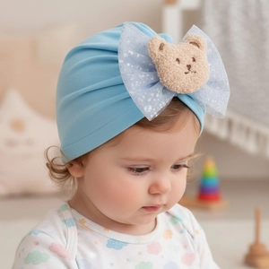 Détail d'un bonnet turban pour bébé avec nœud en maille bleu clair et petit ours 3D