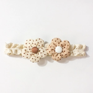 Detail of white lace baby headband with two floral fabric decorations and polka dots