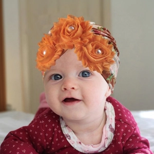 Detailed close-up of baby floral turban hat featuring orange fabric flowers and pearls