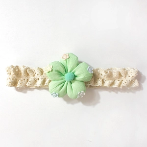 Détail d'un bandeau en dentelle pour bébé avec fleur en tissu vert menthe et broderies