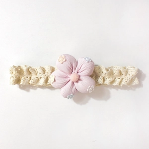 Détail d'un bandeau pour bébé en dentelle avec une grande fleur rose en tissu doux