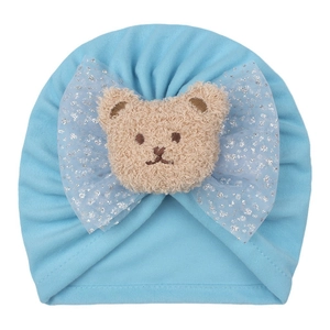 Détail du bonnet bébé avec tête d'ours en peluche et nœud en résille sur tricot bleu