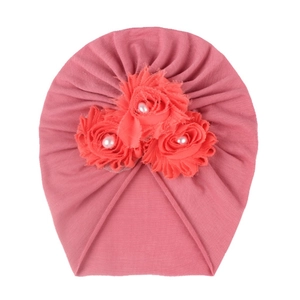Détail de trois roses en tissu avec perles blanches sur bonnet rose pour bébé