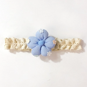Détail d'un bandeau bébé avec broderie florale bleu clair sur un tissu en dentelle beige