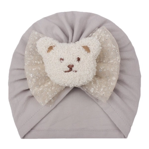 Détail d'un bonnet bébé gris clair avec écusson ours en polaire et nœud en tulle pailleté