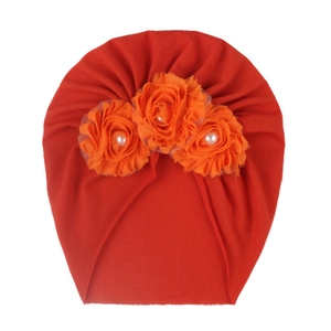 Détail du bonnet turban rouge pour bébé avec trois fleurs en maille orange et perles blanches