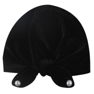 Detail of black velvet baby turban cap featuring a knotted bow with white pearl accents