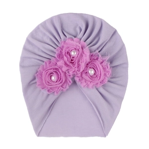 Détail d'un turban lavande pour bébé avec trois roses en tissu rose et perles