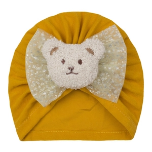 Détail du bonnet en tricot jaune moutarde pour bébé avec nœud pailleté et ours en peluche