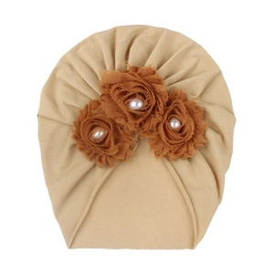 Détail du bonnet turban pour bébé avec trois fleurs en tissu marron et perles sur tricot beige
