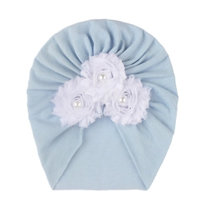 Détail d'un turban pour bébé avec trois fleurs en tissu blanc et perles bleu clair