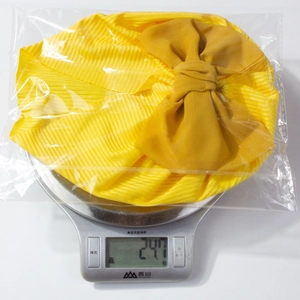 Vue détaillée montrant le poids d'un bonnet jaune pour bébé avec nœud sur une balance à 24,7g