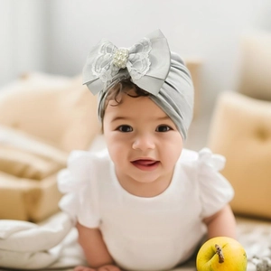 Detail of baby turban hat with light grey ribbed bow, lace trim and pearl bead center
