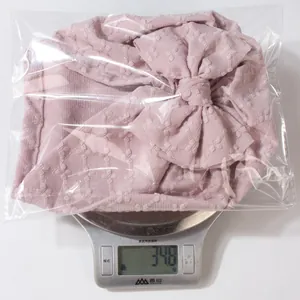 Pink knotted baby hat with bow shown on digital scale weighing 34.8 grams for accuracy
