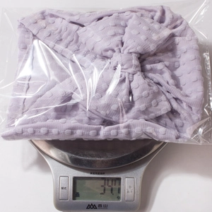 Detail view of a purple polka dot baby beanie with bow on a scale weighing 34.1g