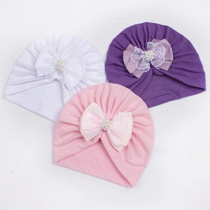Detailed view of baby turban hats with large ribbon bows, lace, and pearls in three colors