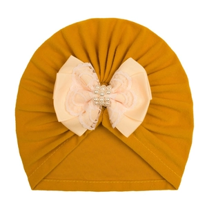 Detail of baby turban hat with ginger yellow knit fabric, lace bow, and faux pearls