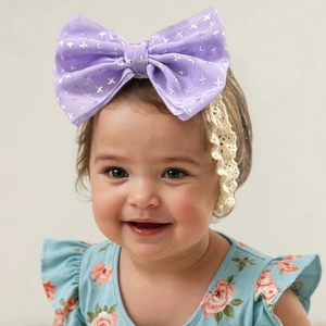 Détail d'un bandeau bébé avec un grand nœud violet, imprimé argenté et bordure en dentelle