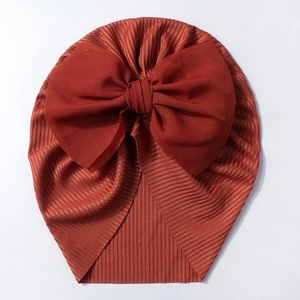 Détail du turban pour bébé avec texture en maille côtelée et grand nœud en mousseline rouge