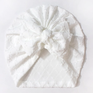 Detail of baby turban hat featuring white jacquard fabric and a large layered bow