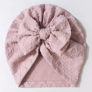 Detailed close-up of a pink baby beanie with a large bow and 3D textured waffle pattern