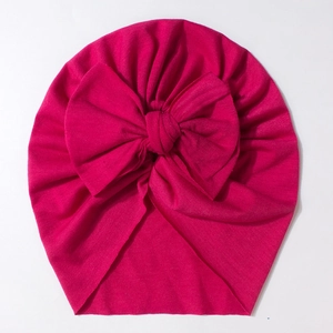 Detail of soft rose red baby turban hat featuring a large decorative bow and pleated knit